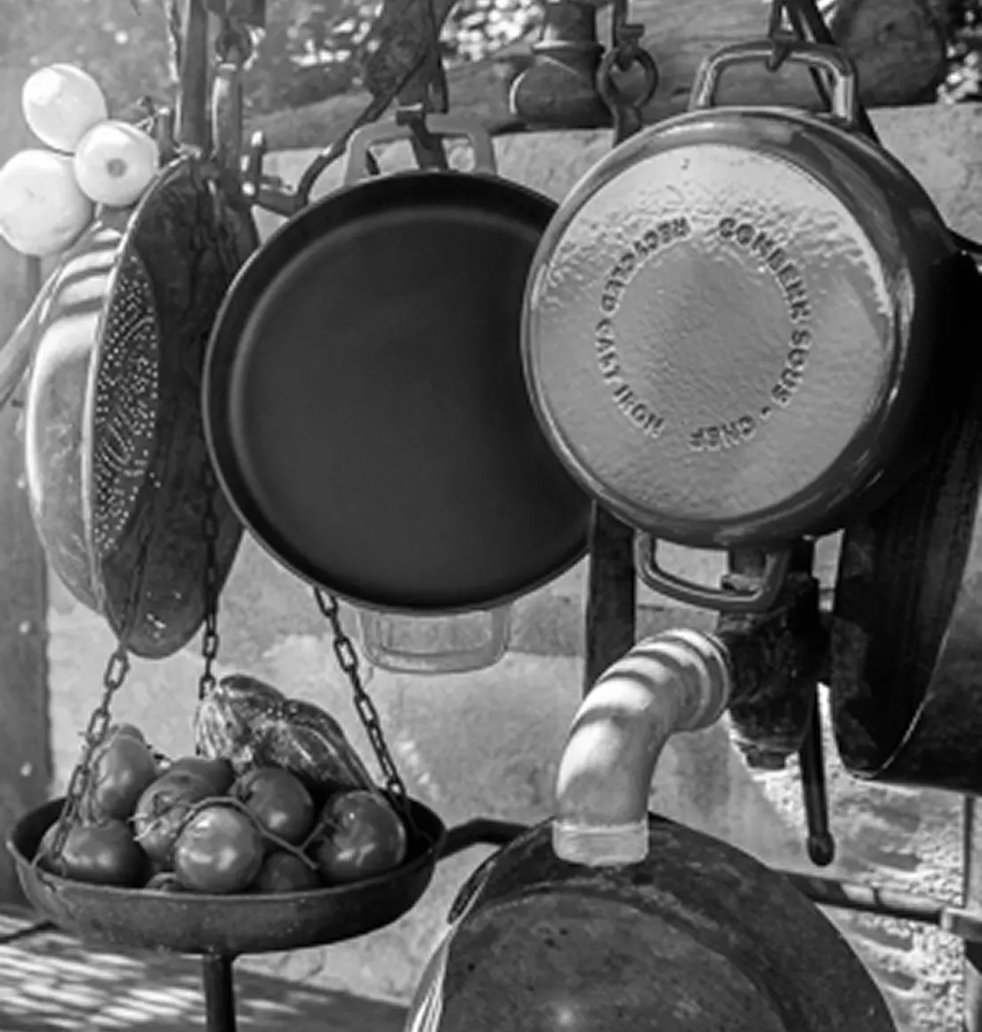 Gietijzeren COMBEKK-pannen hangen aan haken boven een schaal met verse tomaten.