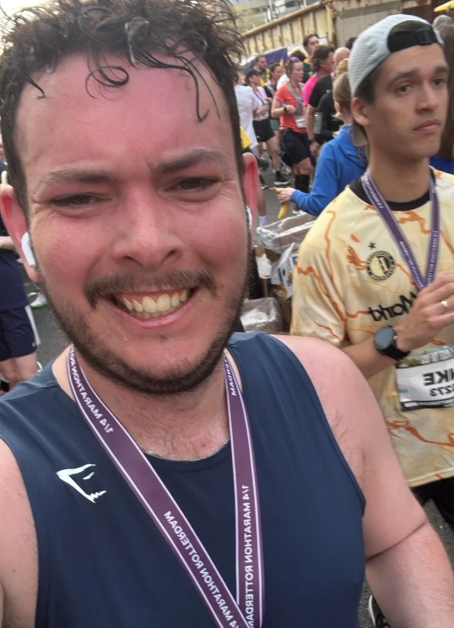 Joris maakt een selfie na het voltooien van de Rotterdam Marathon, met zijn medaille om zijn nek en andere hardlopers op de achtergrond.