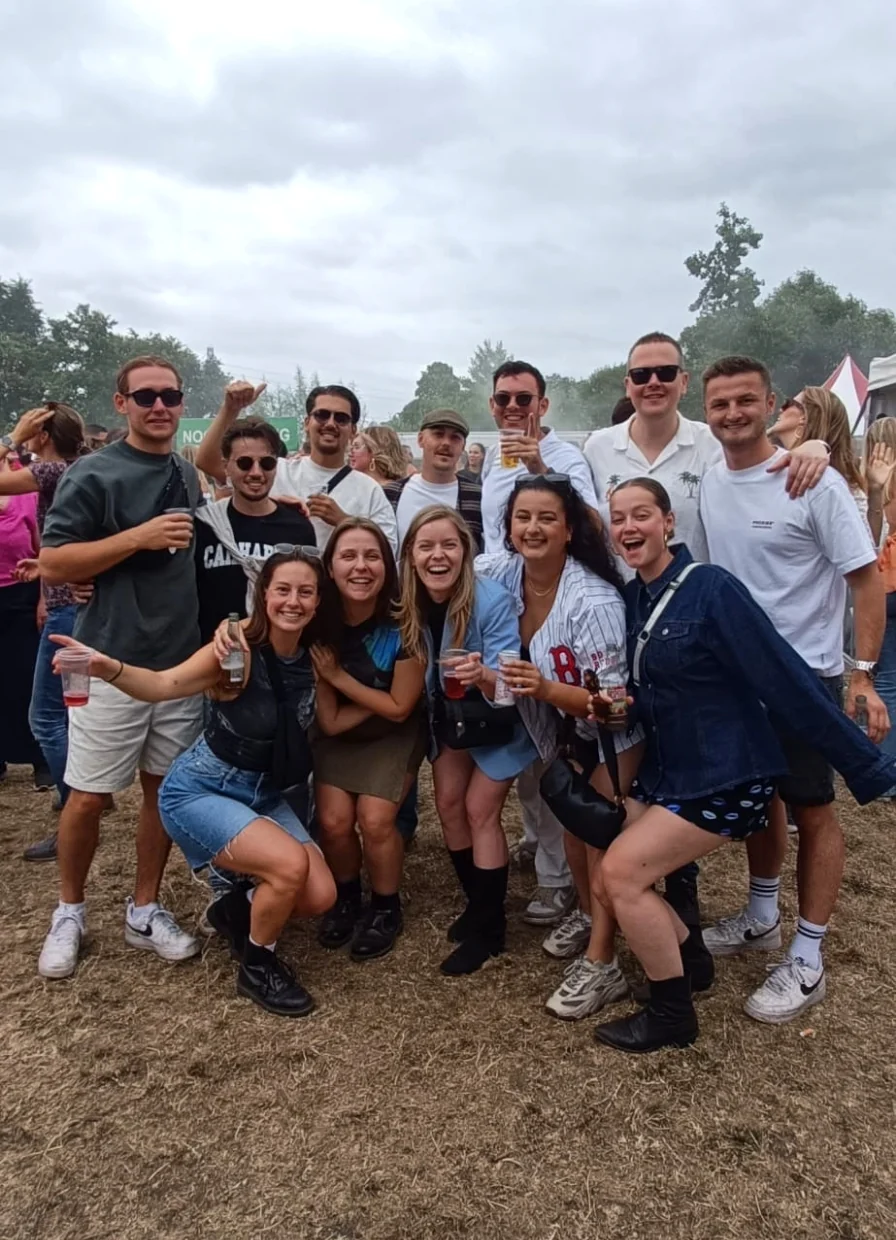 Groep vrienden poseert lachend met drankjes op een openluchtfestival.